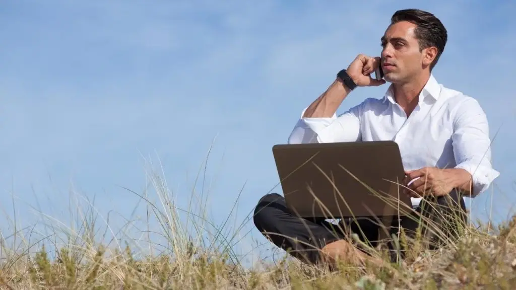 Hombre trabajando en remoto desde la naturaleza con portátil, representando los gastos del teletrabajo.